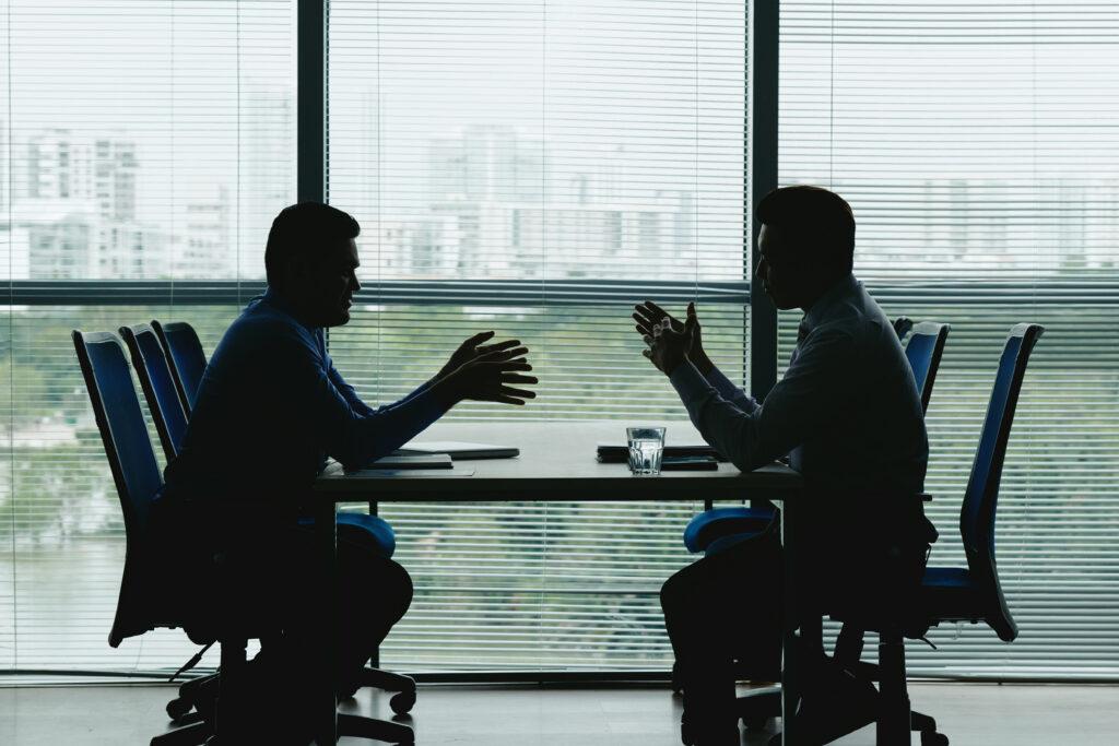 Silhouettes of business people sitting at table against the office window and discussing various issues- small business